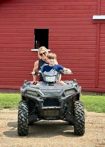 Lisa and her son on an ATV in front of a red barn