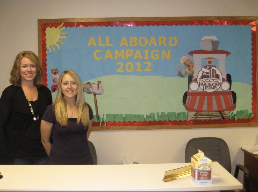 Lisa Romkema and Christina Riss next to the 2012 Imagination Library bulletin board. 