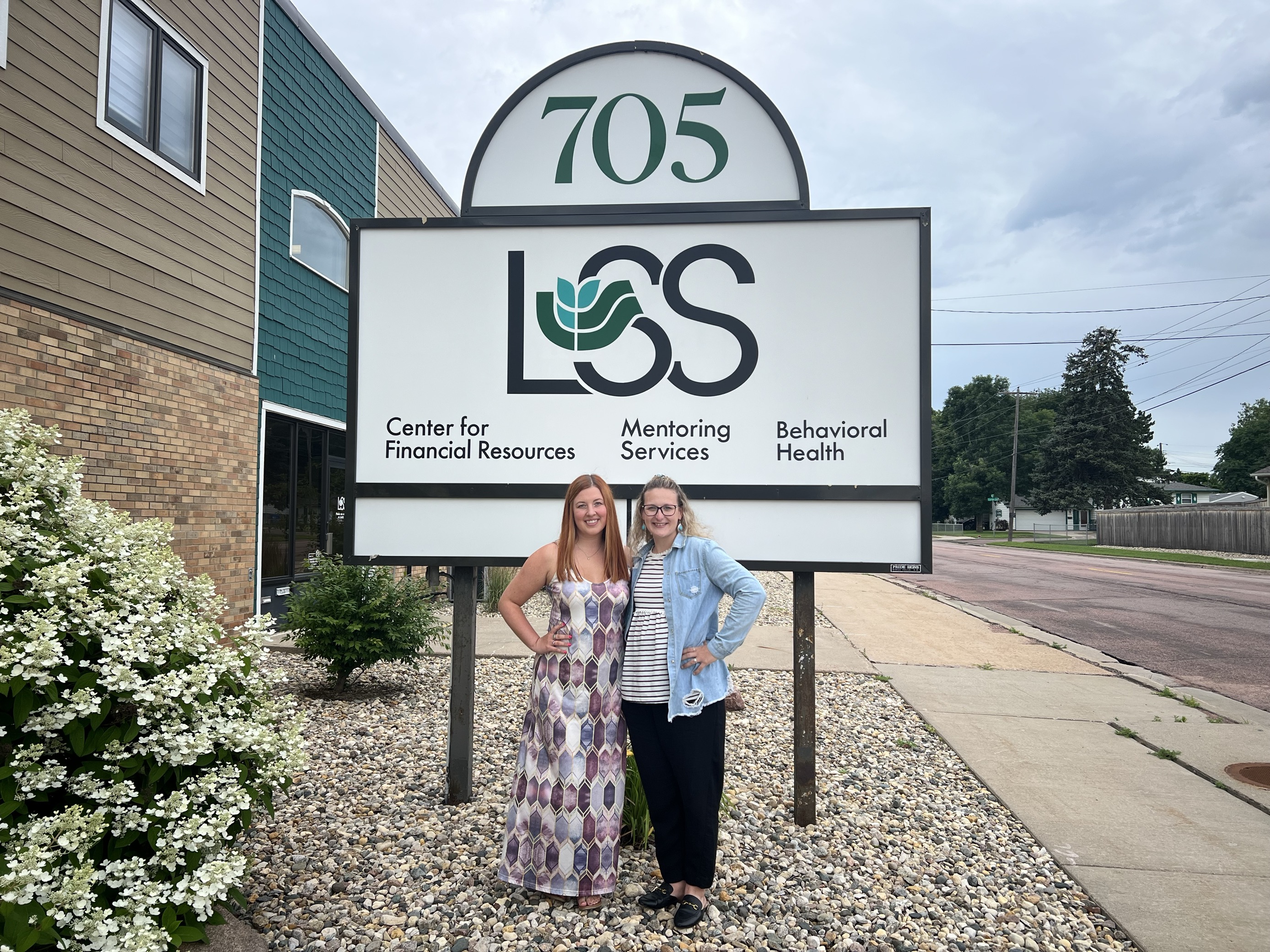 Rachael and Jill, SEUW Staff, standing in front of LSS Mentoring sign outdoors.