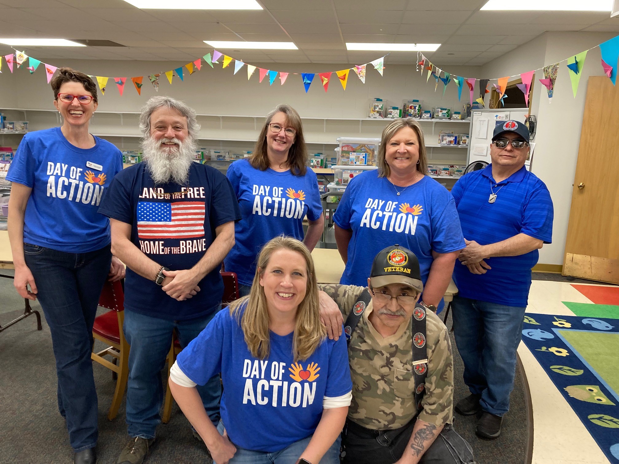 Adrienne McKeown and five other volunteers posing with Coscioni at Toy Lending Library wearing Day of Action shirts. 